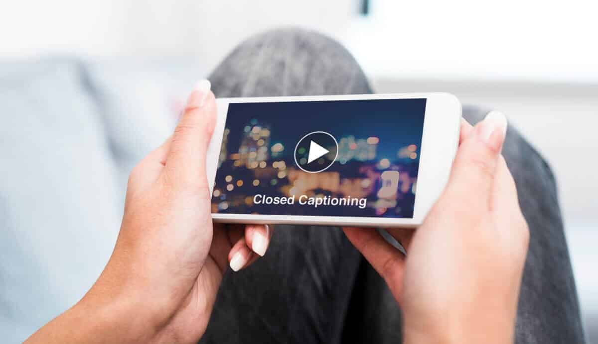 Person holding smartphone displaying a video with "Closed Captioning" text, emphasizing the importance of captions for video engagement on social media.