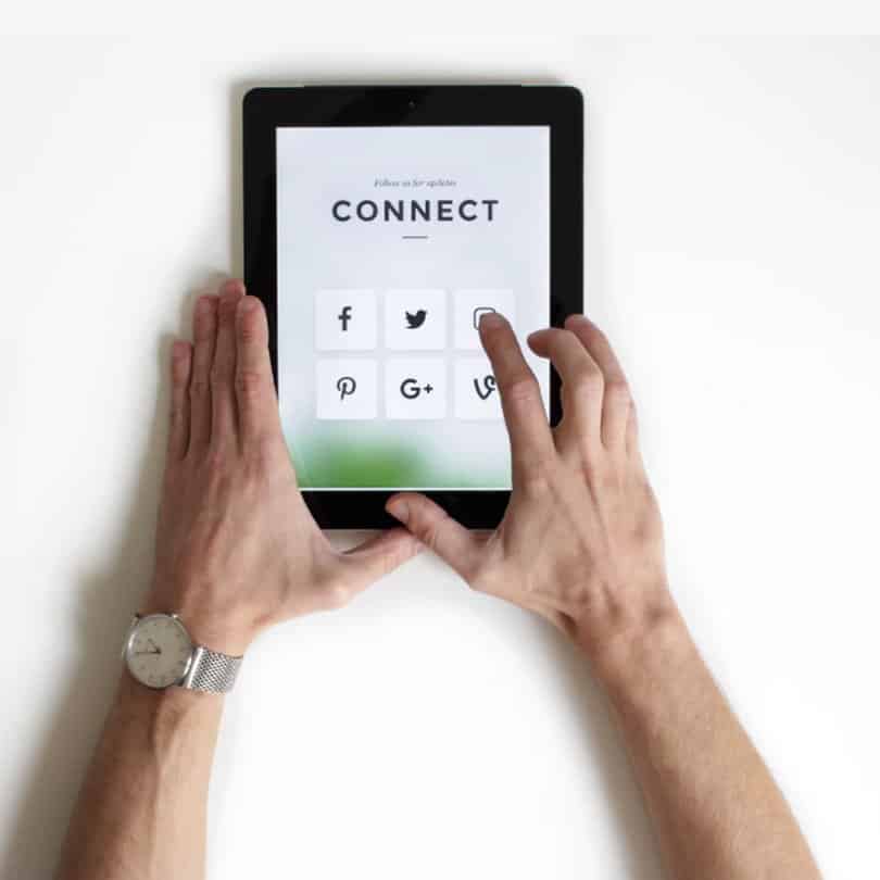 Hands interacting with a tablet displaying social media icons and the word "CONNECT," emphasizing digital engagement and brand presence.