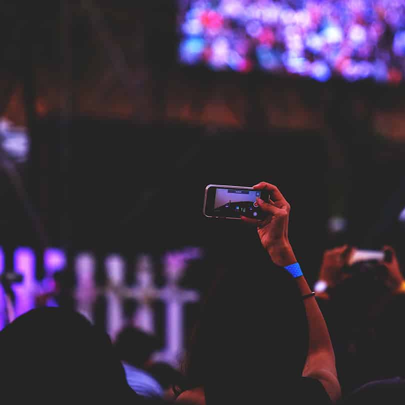 Person holding a smartphone to capture live video at a social media event, emphasizing real-time engagement and connection.
