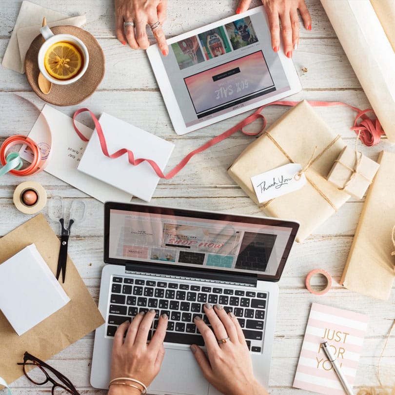 Hands typing on a laptop surrounded by spring-themed marketing materials, a tablet displaying digital content, and a cup of tea with lemon, emphasizing seasonal trends in digital advertising and consumer engagement.