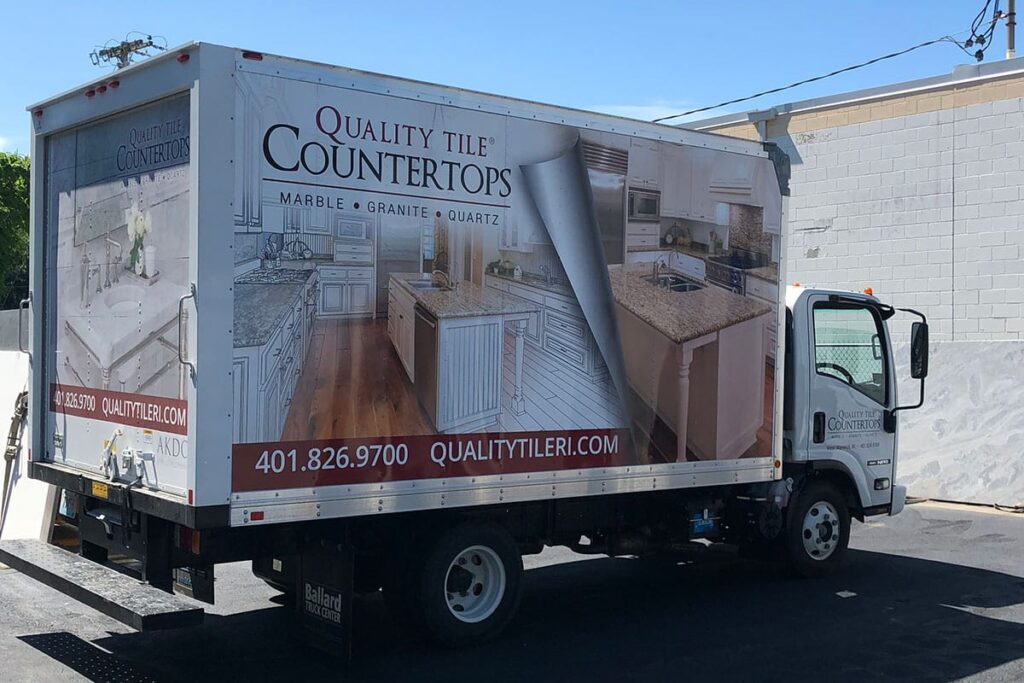 Quality Tile Countertops delivery truck featuring images of marble, granite, and quartz countertops, showcasing kitchen designs and contact information for QualityTileRI.com.