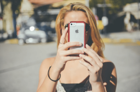 Woman taking a selfie with smartphone in outdoor setting, reflecting social media engagement trends.