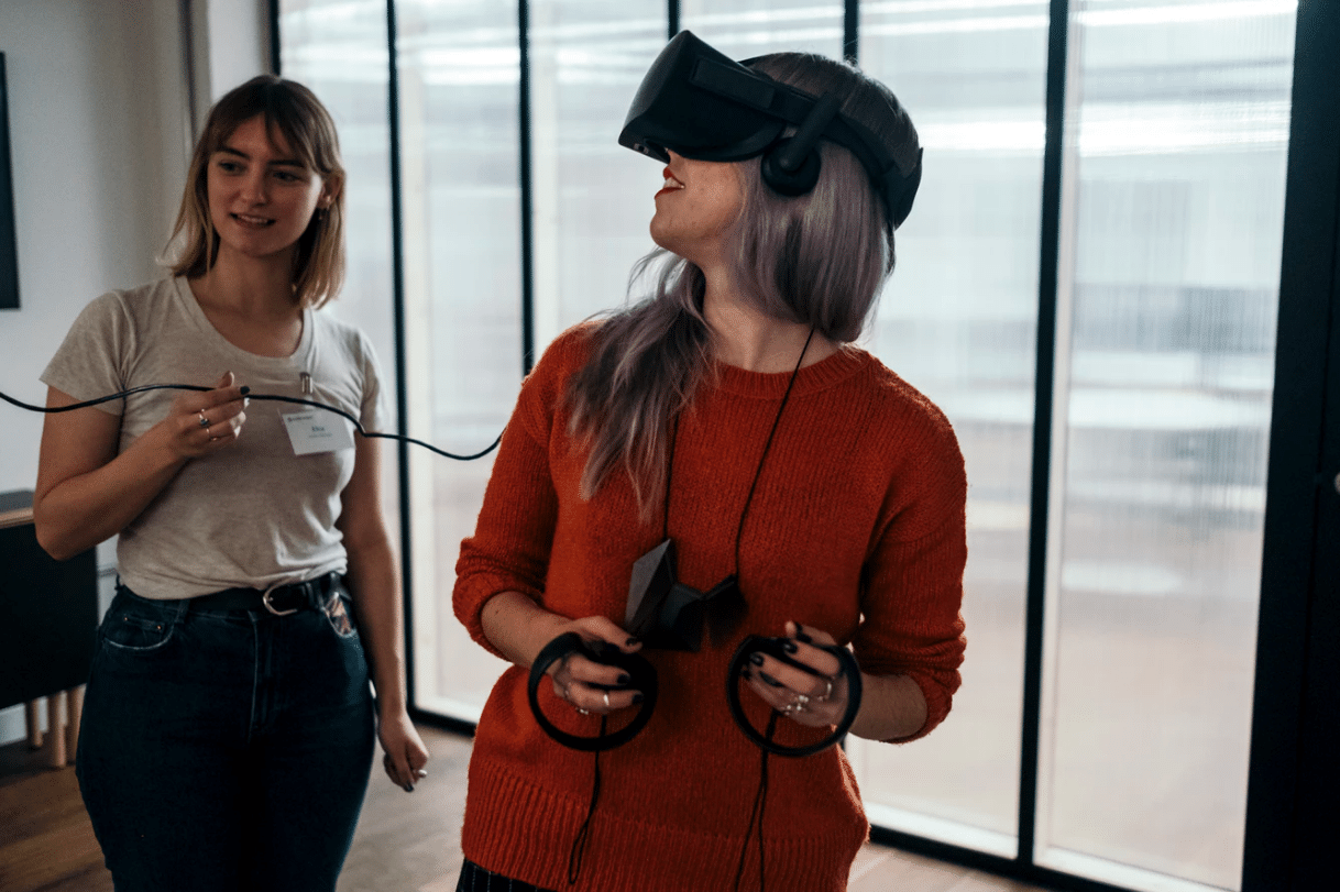 Woman wearing virtual reality headset engaging with technology, while another woman assists, illustrating augmented reality trends in marketing.