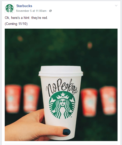 Starbucks holiday cup with "No Peeking" written on it, surrounded by blurred red cups, promoting seasonal marketing strategies.